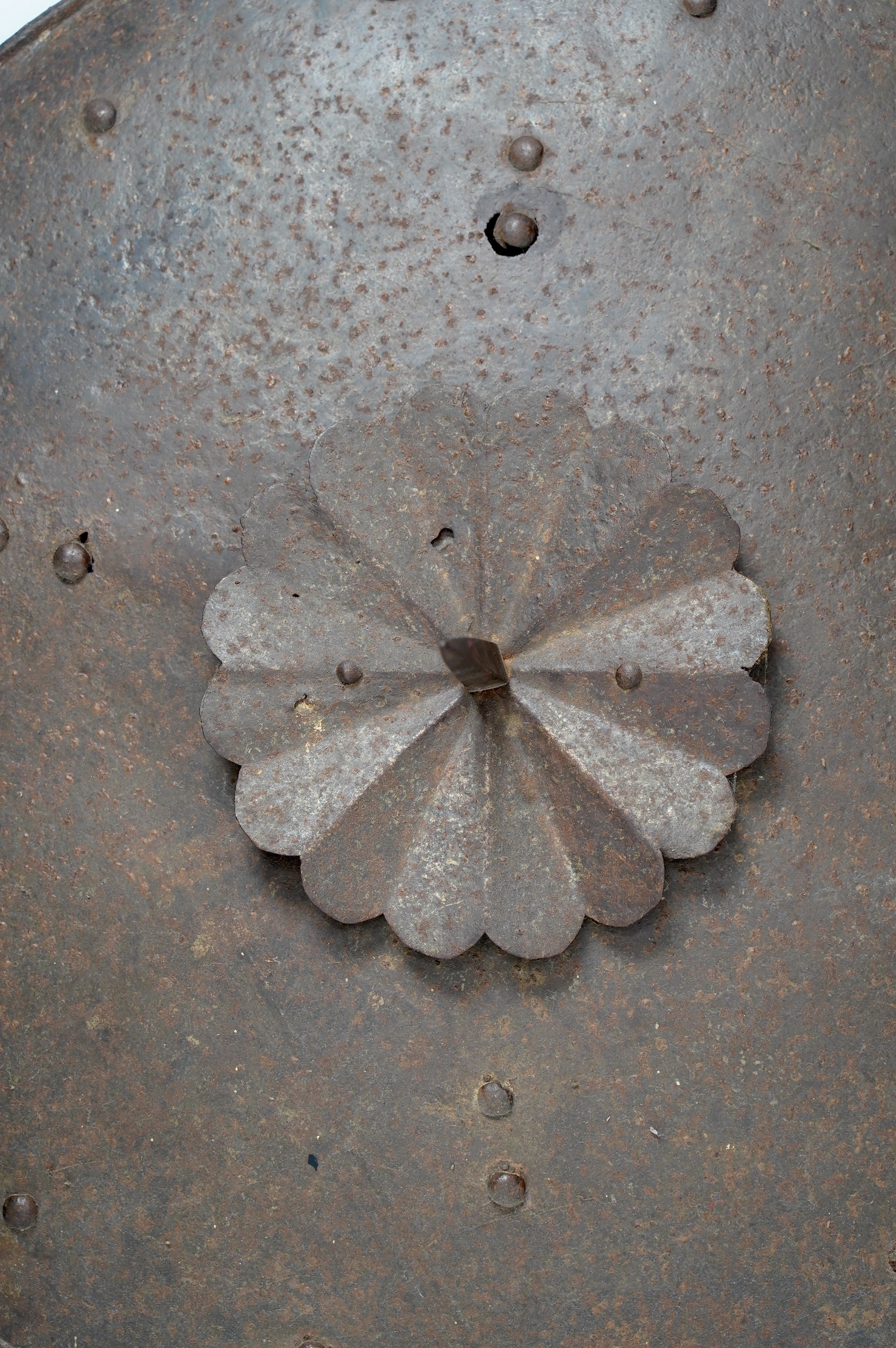 A 19th century iron shield with centre spike, formally part of a suit of armour, 57.5cm diameter. Condition - poor, surface rust and pitting overall